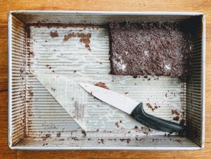 9" x 13" cake pan lined with parchment, part of a chocolate cake still in the pan, parchment covered with crumbs and stained with grease.